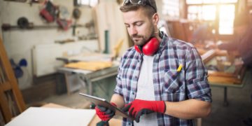 carpintero joven trabajador profesional gafas protectoras sosteniendo tableta comprobando diseno su proyecto taller