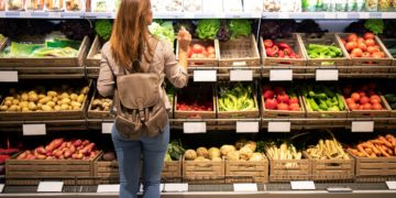 good looking woman standing front vegetable shelves choosing what buy